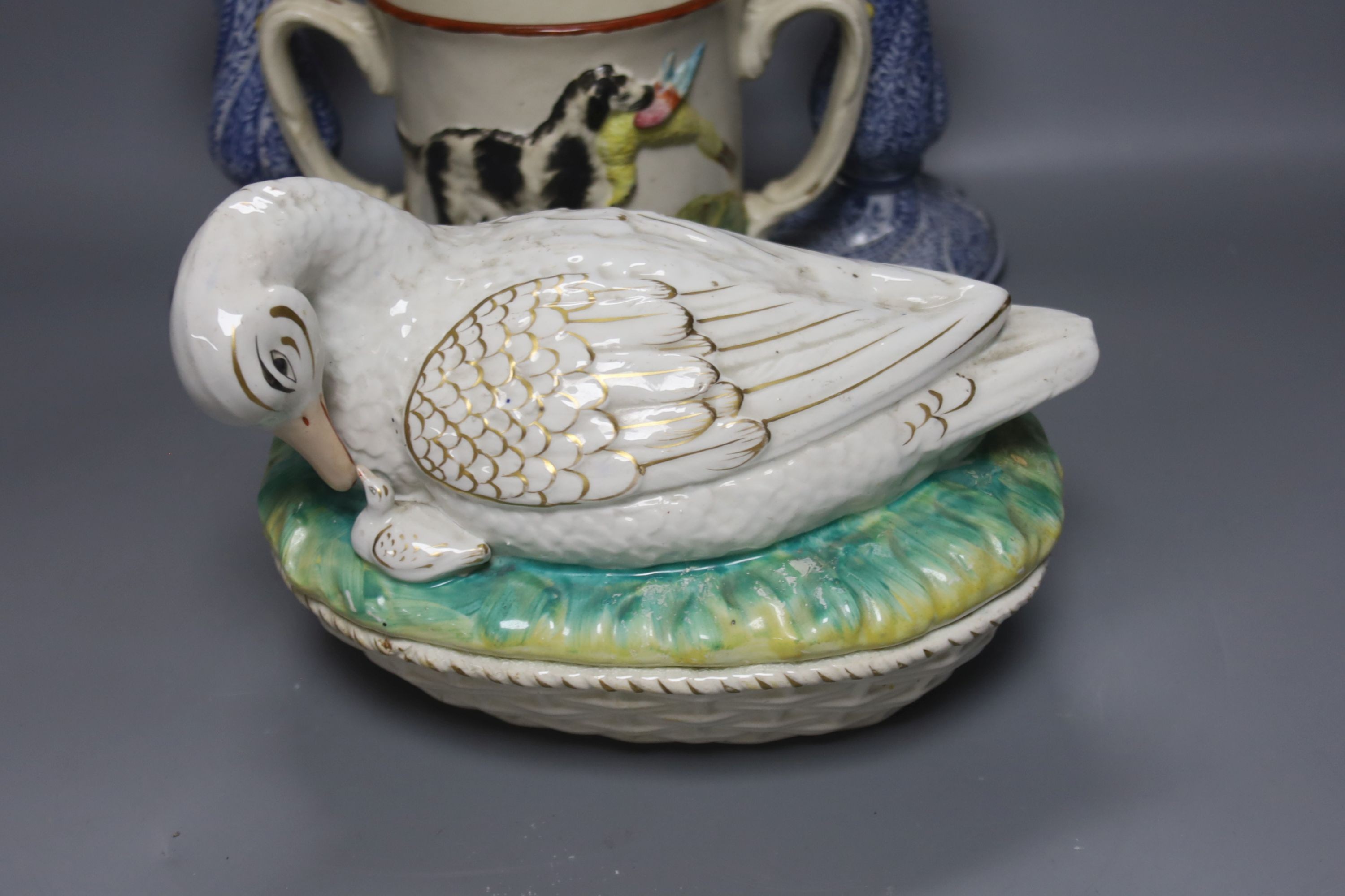 A Staffordshire pottery ‘duck’ tureen and cover, 23cm, a pair of faience candlesticks, Staffordshire figures of dogs, sheep and a zebra and a two handled loving mug